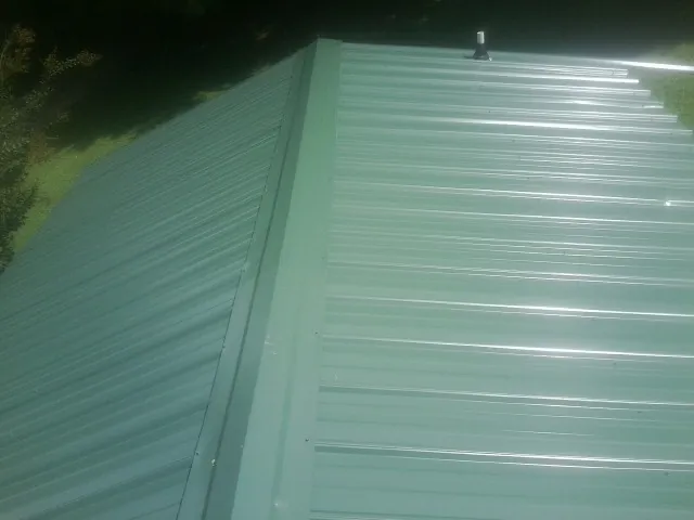 New green metal panels meeting at the ridge of a roof — Flat Roof Repair work by our crew in Balch Springs