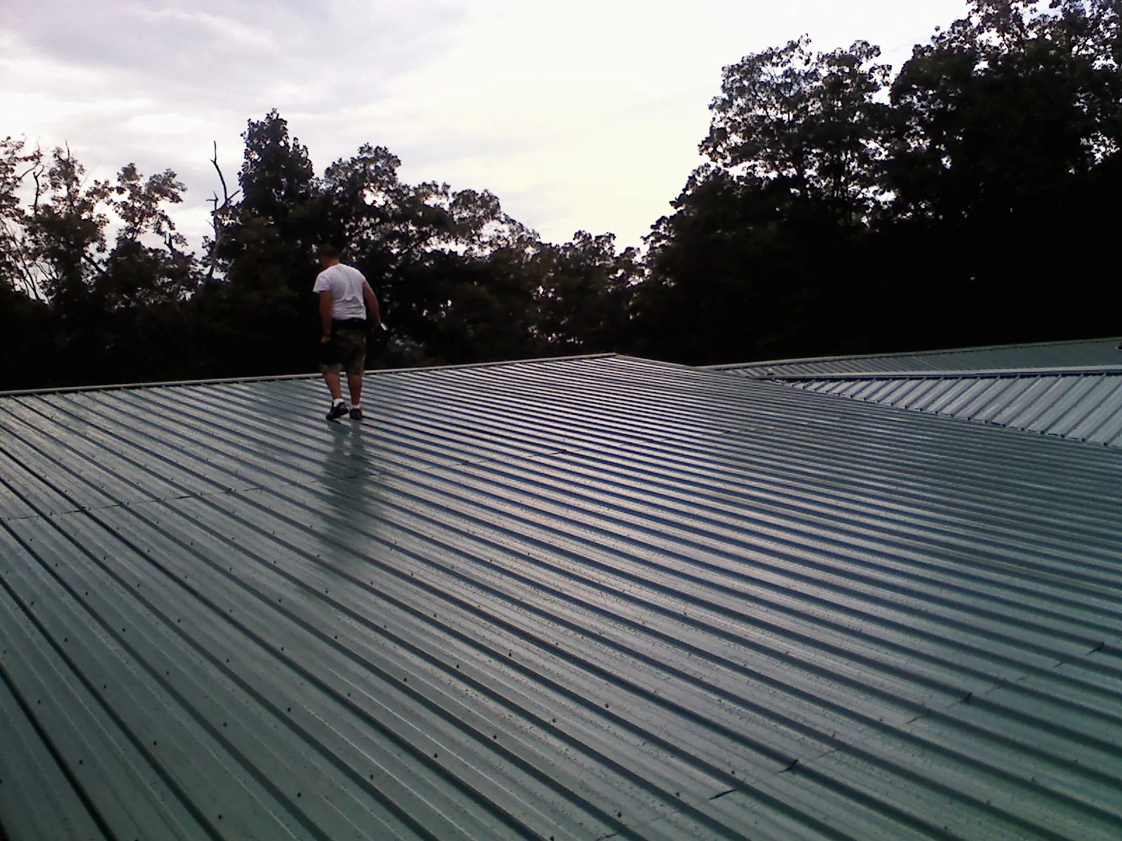 Roofer walking a wide expanse of new green metal roofing in Balch Springs