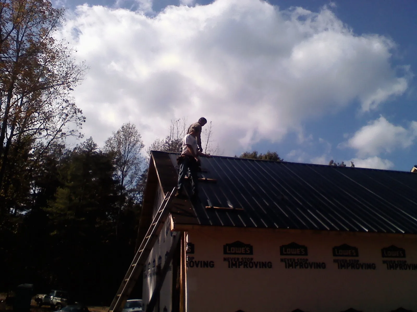 Roofer fastening dark metal panels high against a cloudy sky, from a Roof Inspection job in Balch Springs