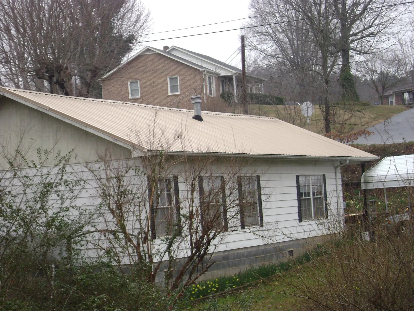 Tan metal roof on a white sided house set into a hillside — Commercial Roofing by Roofing Brothers in Balch Springs